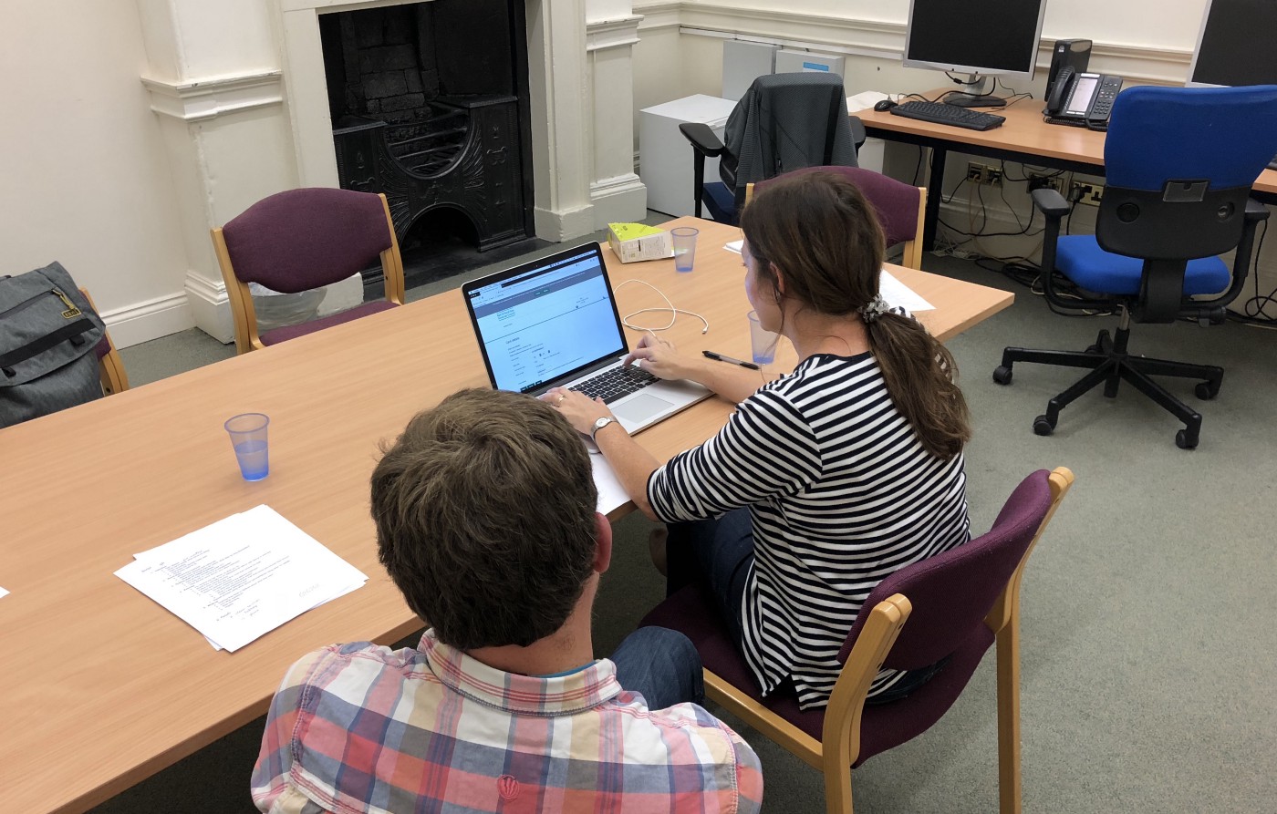 A woman using a computer whilst a man observes what she is doing