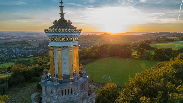 An elevated view of Beckford’s Tower at sunset, with golden light on the tower and green fields and trees stretching into the distance