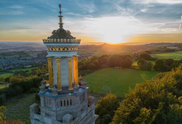 An elevated view of Beckford’s Tower at sunset, with golden light on the tower and green fields and trees stretching into the distance