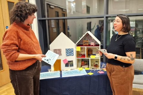 Two ladies having a discussion in front of a model of a house