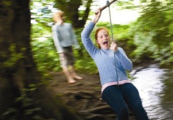 Girl on rope swing over stream