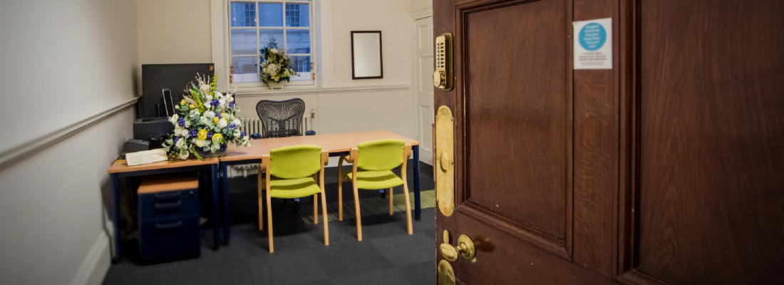 Registrar room with door open to the left and a desk and two green chairs in front of a desk